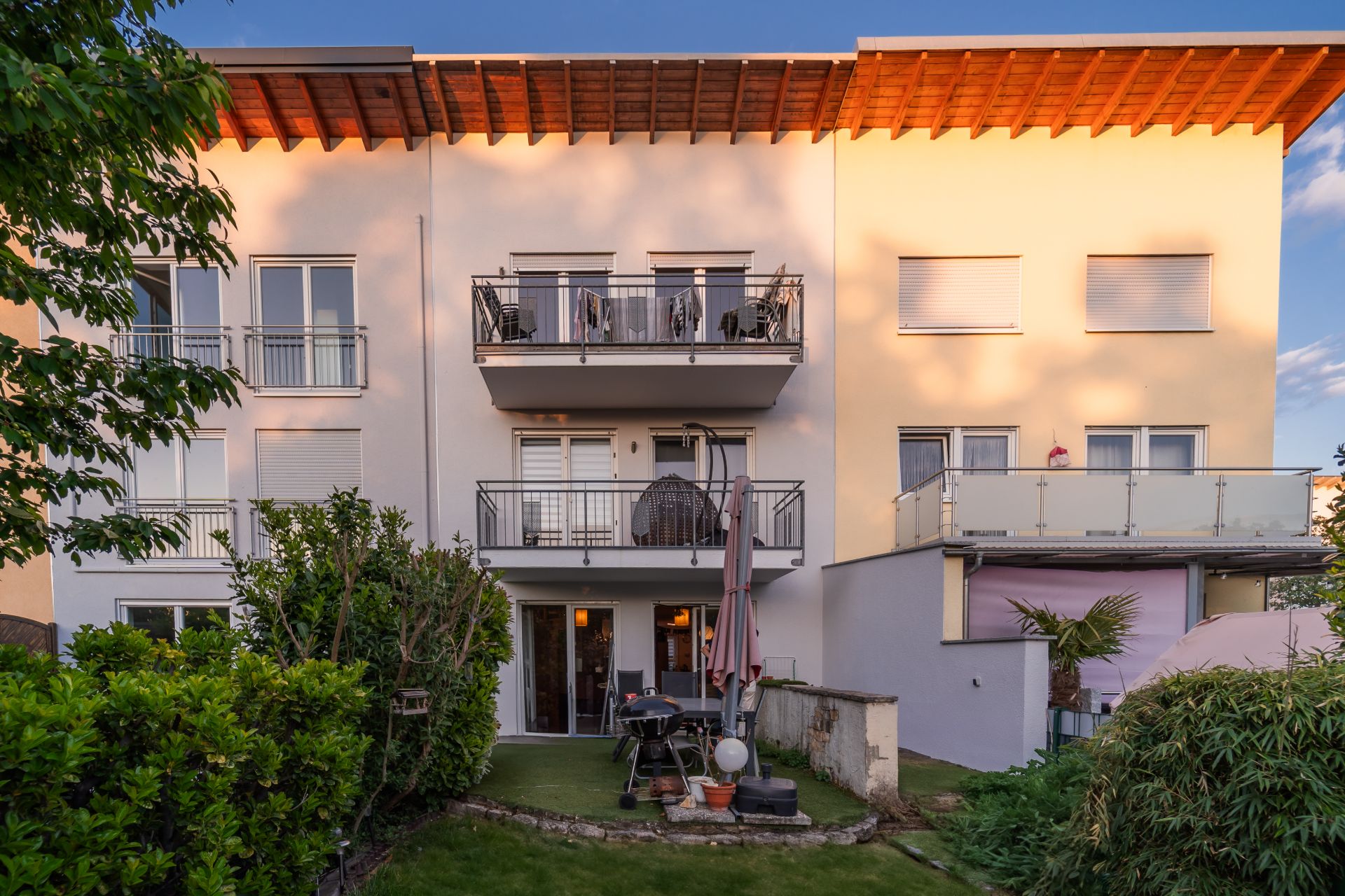 Moderne Wohnhausfassade mit zwei Balkonen, Terrasse und Garten im Vordergrund.