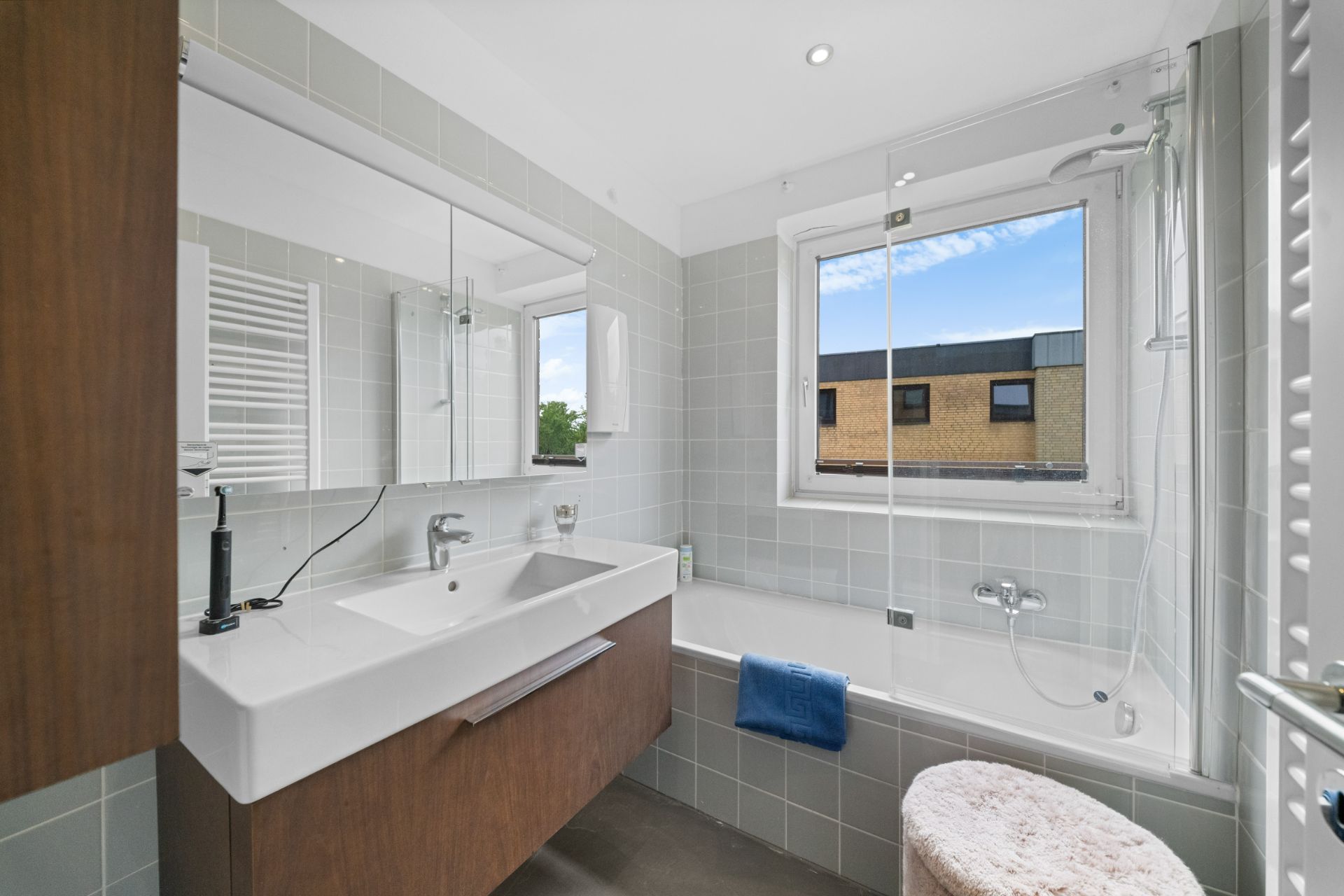 Modernes Badezimmer mit Waschbecken, Spiegel, Badewanne und zwei Fenstern.