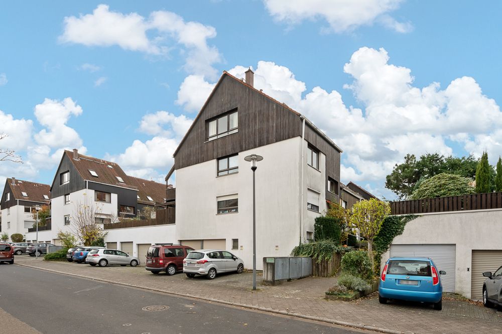 Mehrfamilienhäuser mit Garagen und parkenden Autos an einer Wohnstraße, Bäume und Lampenmast sichtbar.