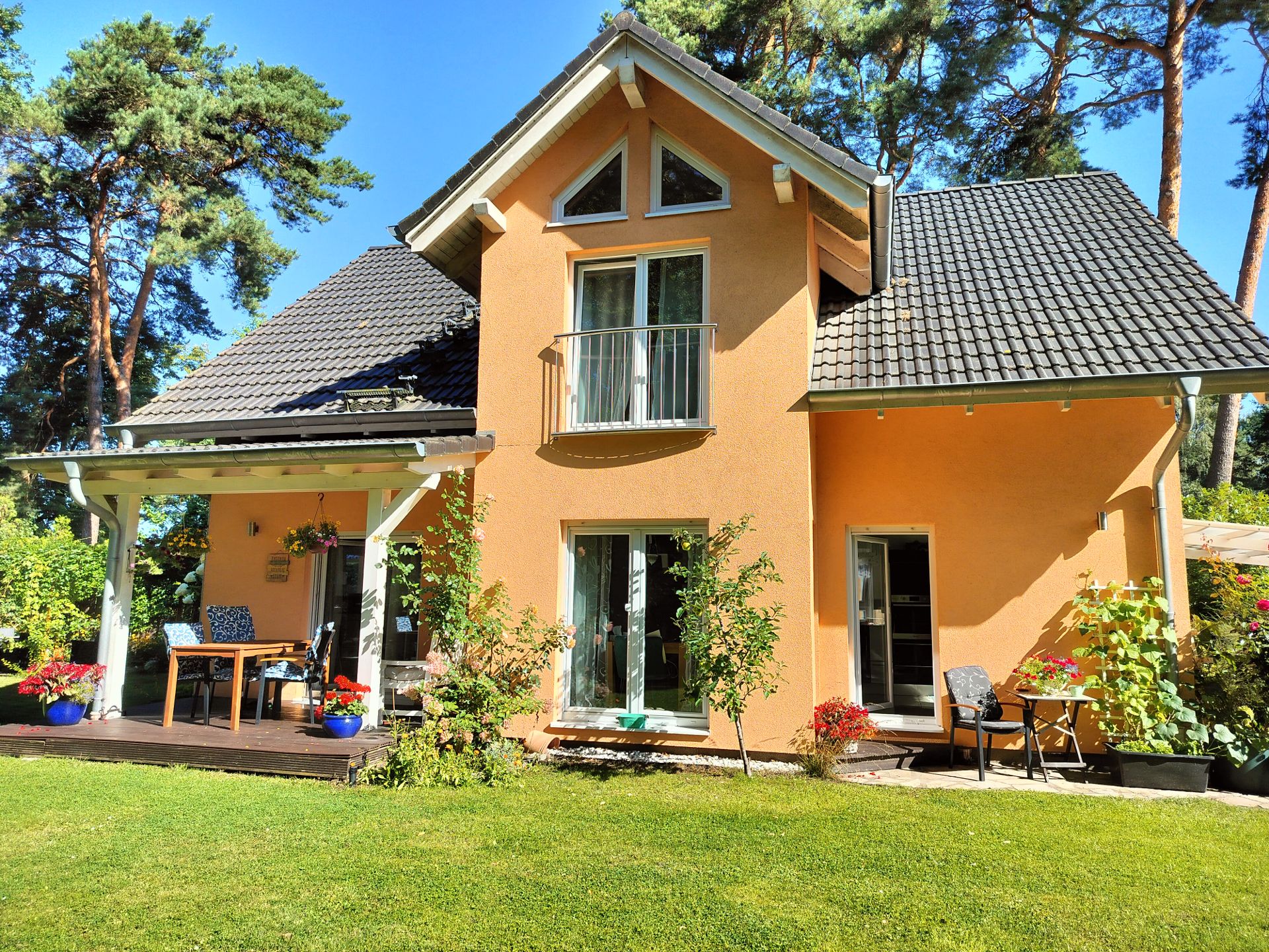 Modernes Einfamilienhaus mit orangefarbener Fassade, Balkon und Terrasse im Garten, umgeben von Bäumen.