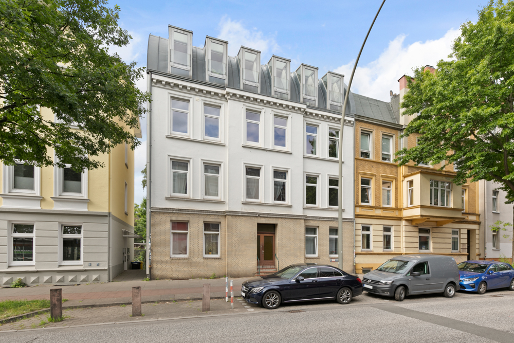 Mehrstöckiges Wohnhaus mit hellen Fassaden und parkenden Autos auf der Straße.