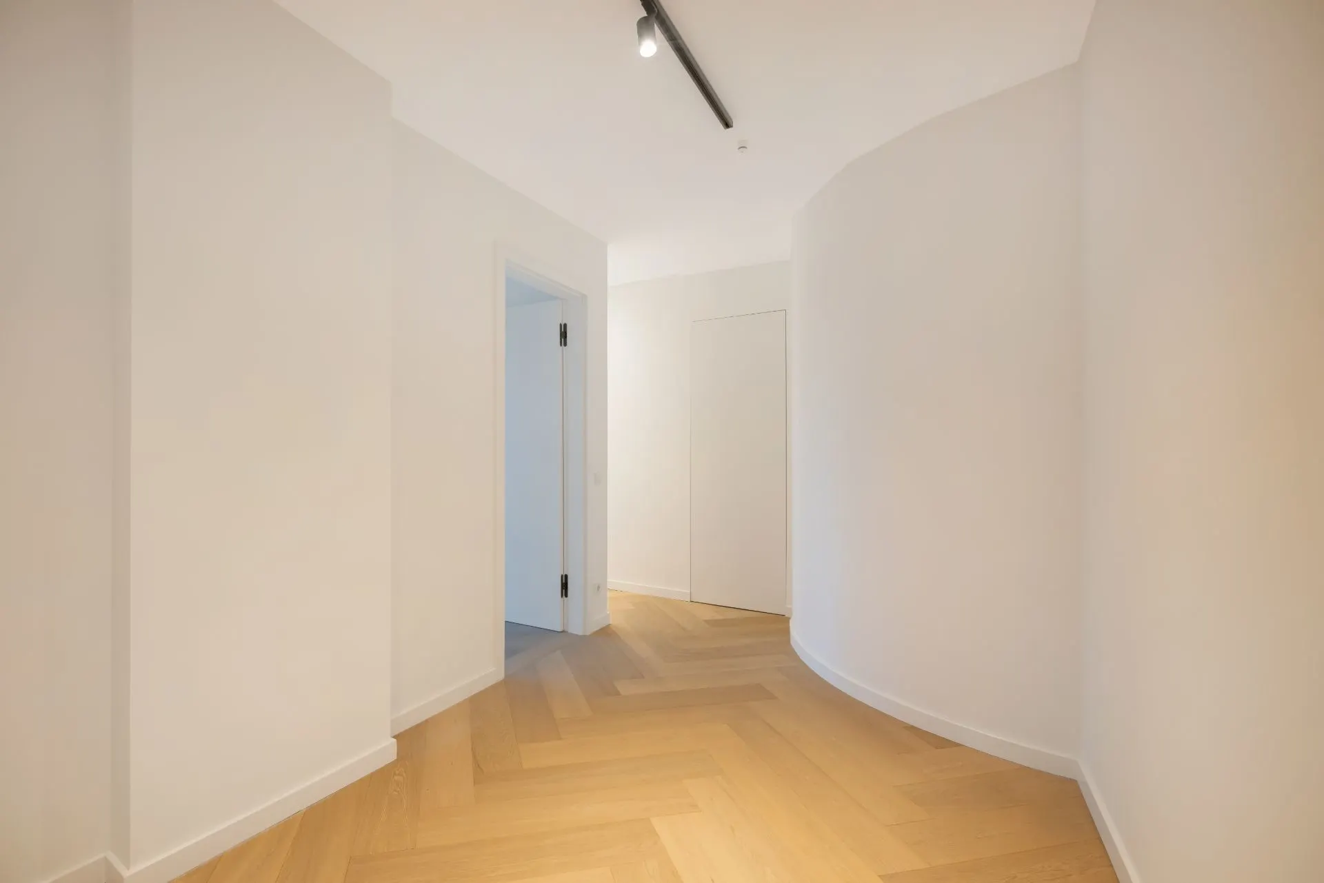 Heller Flur mit Holzboden, weißen Wänden und einer weißen Tür links.