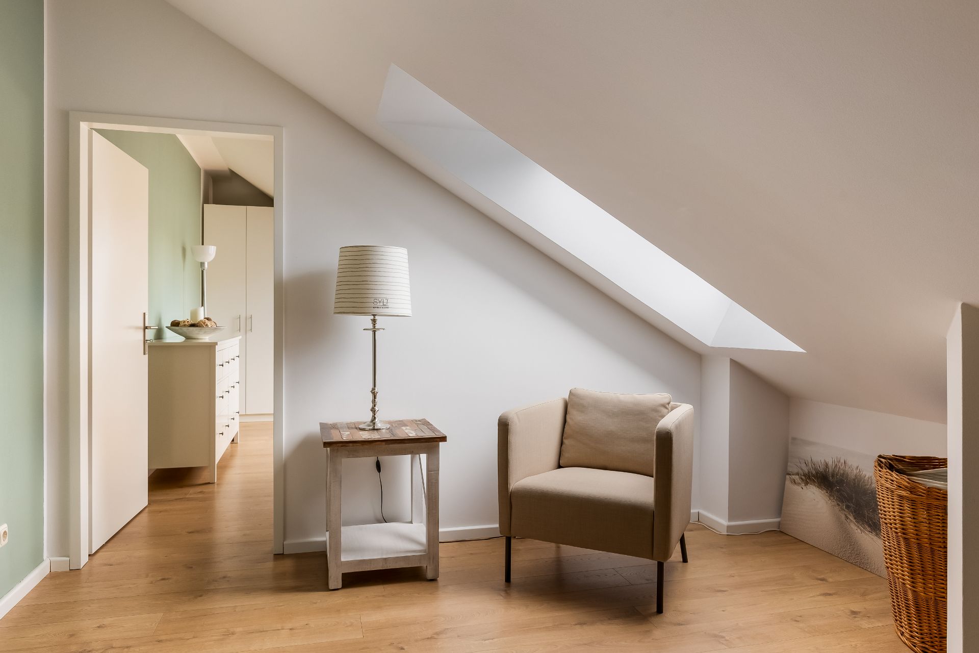 Helles Zimmer mit Sessel, Beistelltisch, Stehlampe und Dachfenster.