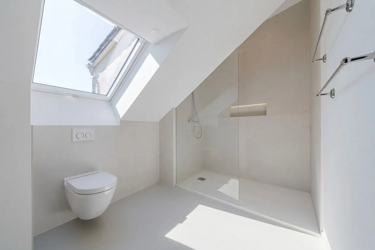 Modernes, helles Bad mit Dusche, WC und Dachfenster unter einer schrägen Decke.