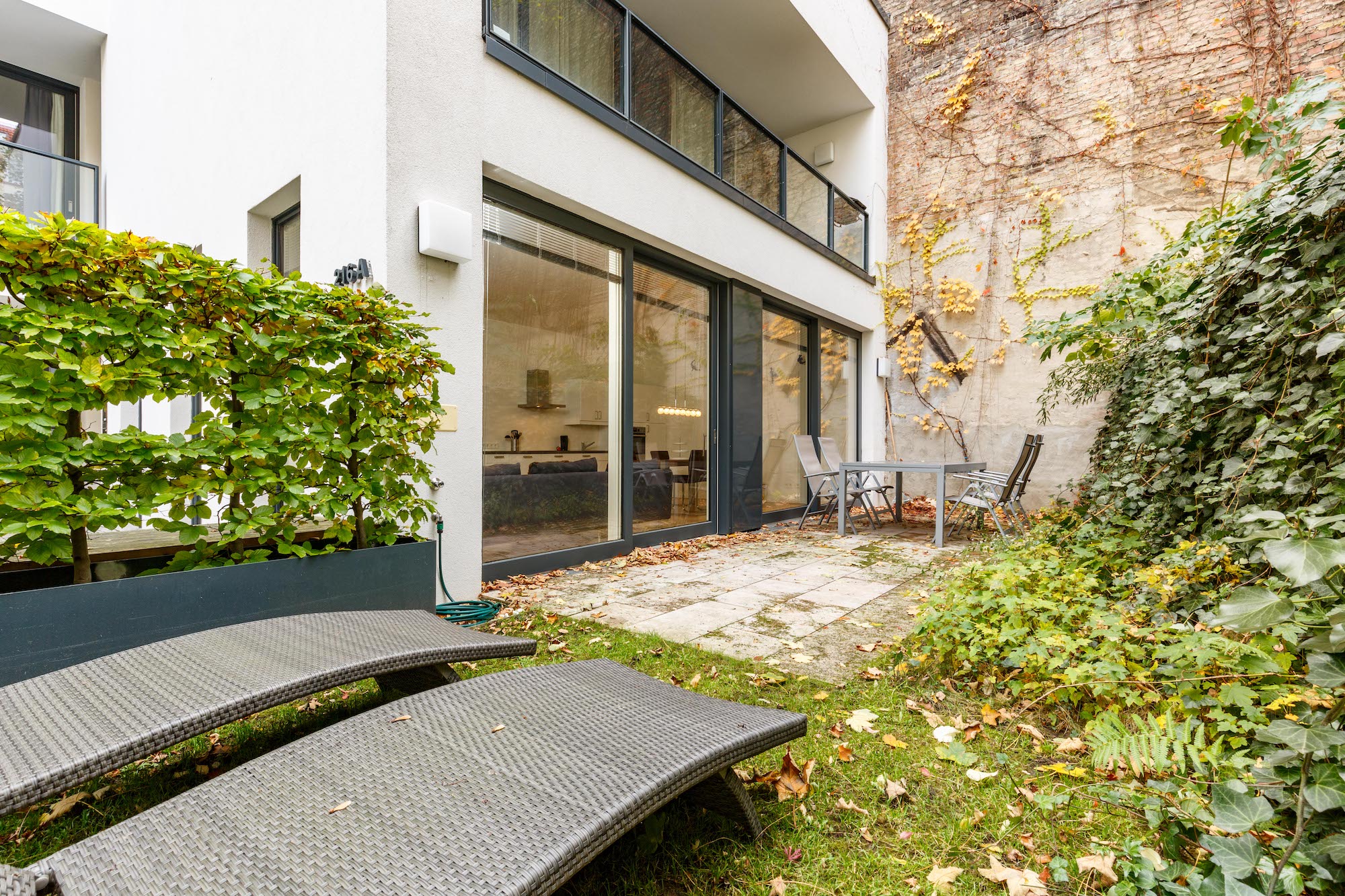 Kleine Terrasse mit Tisch, vier Stühlen und zwei Liegen neben einer modernen Hausfassade.