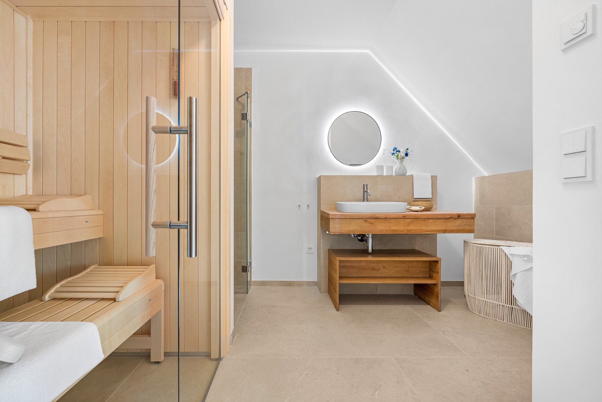Modernes Badezimmer mit Holzsauna, runder Spiegel über dem Waschbecken und Handtüchern.