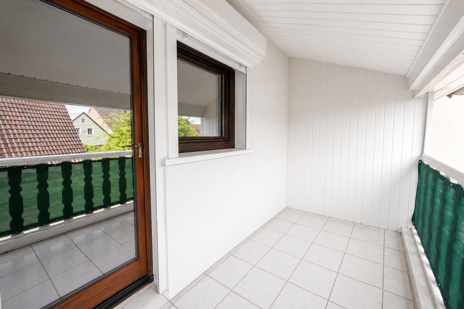 Überdachter Balkon mit Fliesenboden, Fenster und Tür ins Innere, grüne Balkonverkleidung.
