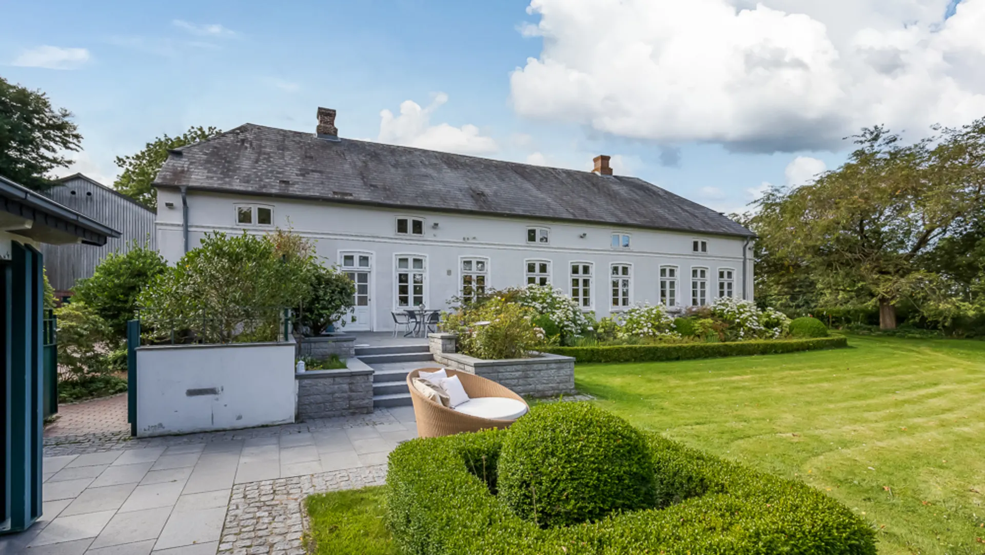 Großes weißes Wohnhaus mit Garten, Terrasse und Sitzbereich im Freien.
