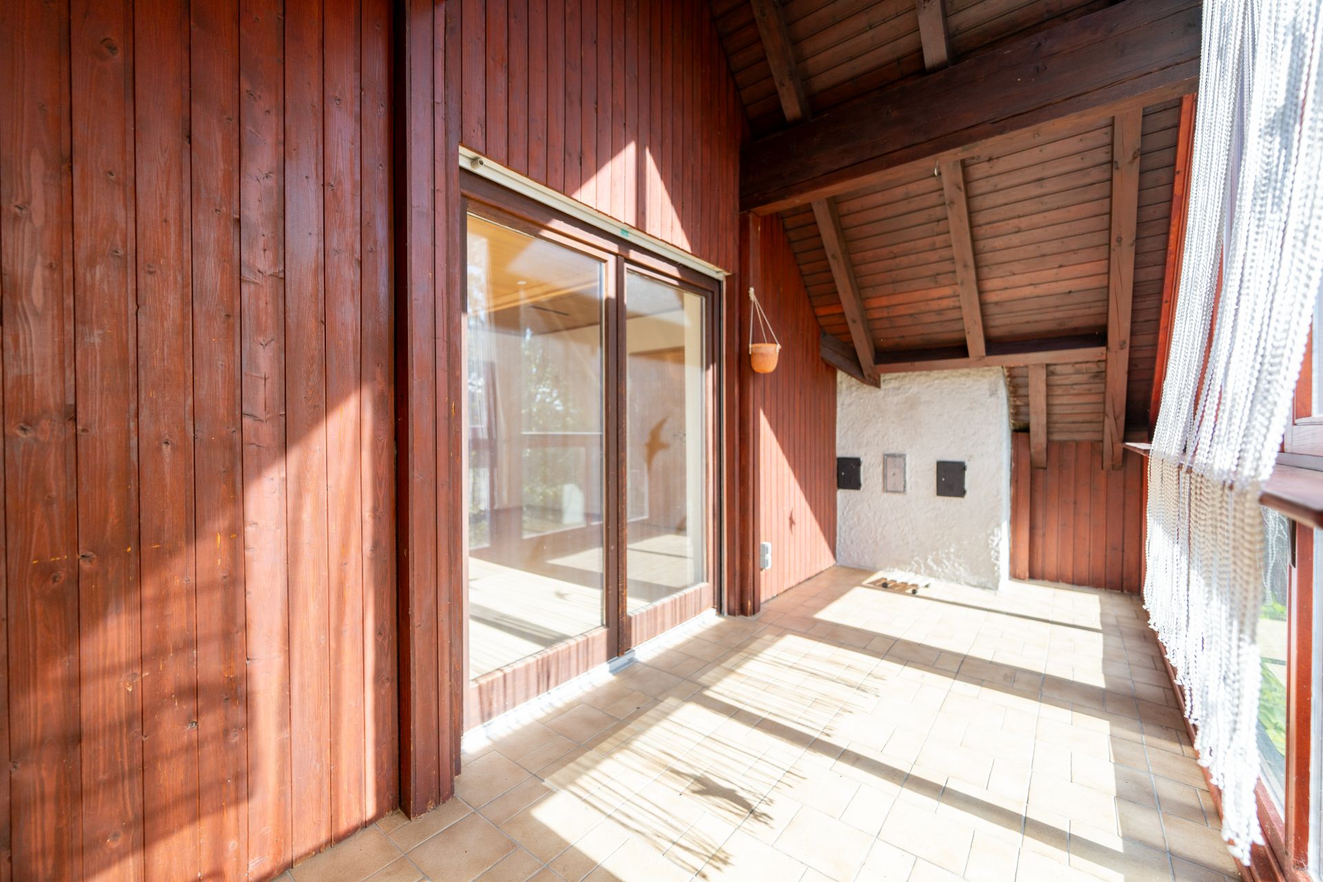 Überdachter Balkon mit Holzverkleidung, Fliesenboden und großen Glas-Schiebetüren.