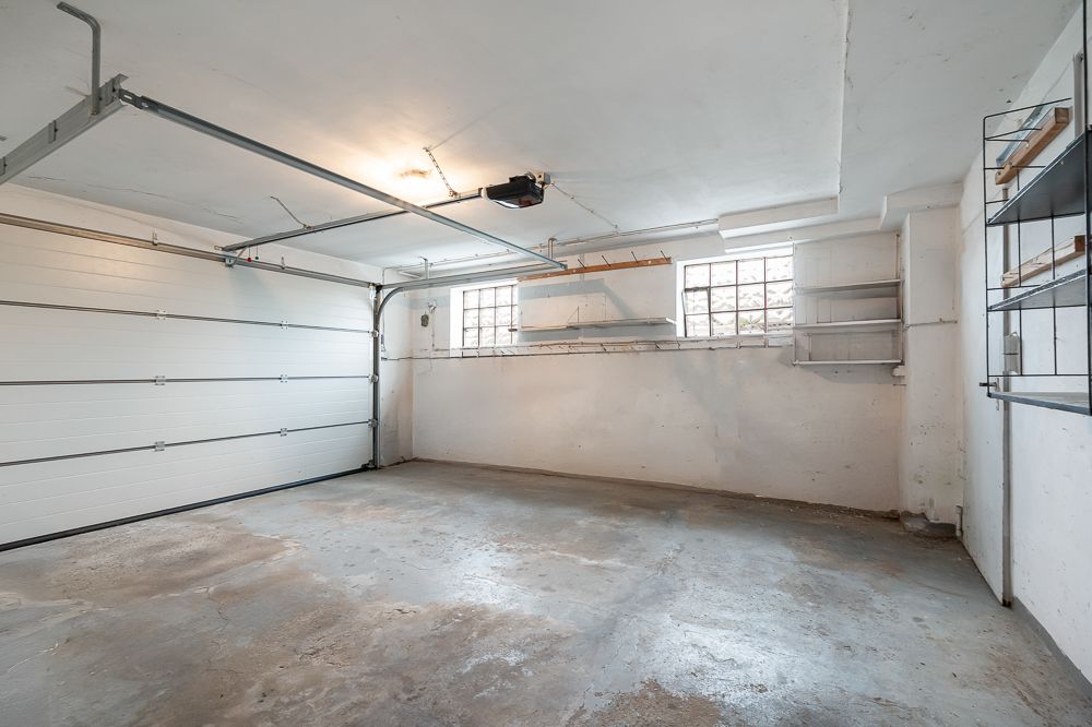 Leere Garage mit zwei Fenstern, Regalen an den Wänden und einem geschlossenen Garagentor.