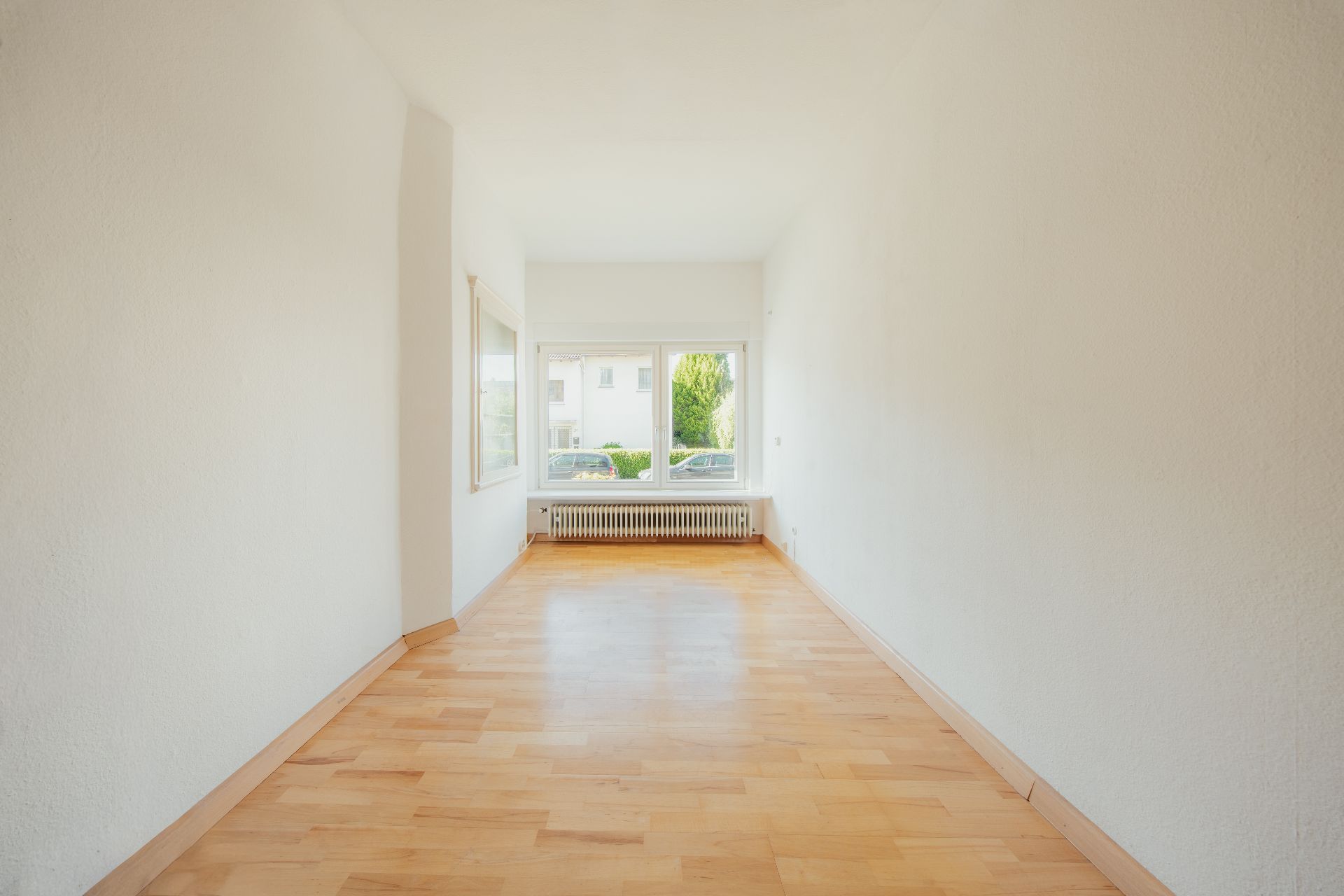 Heller, leerer Raum mit Holzfußboden und großem Fenster mit Blick nach draußen.