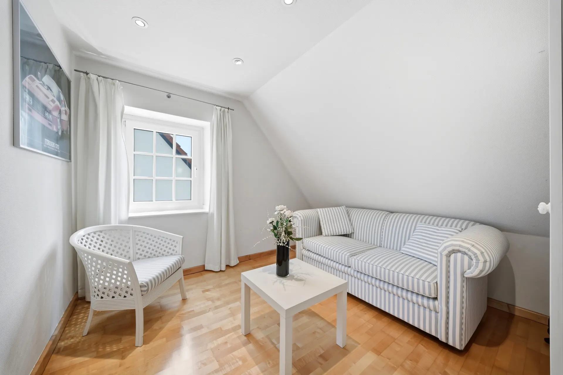Helles Zimmer mit gestreiftem Sofa, weißem Stuhl, Tisch und Fenster mit weißen Vorhängen.