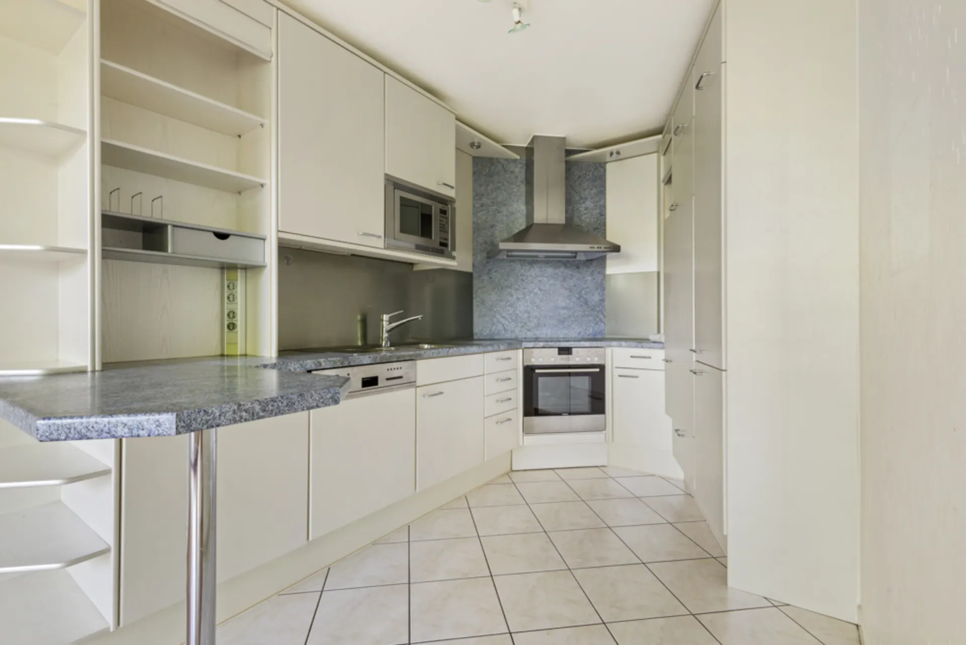 Moderne Einbauküche mit weißen Schränken, Herd, Backofen, Geschirrspüler und Eckarbeitsplatte.