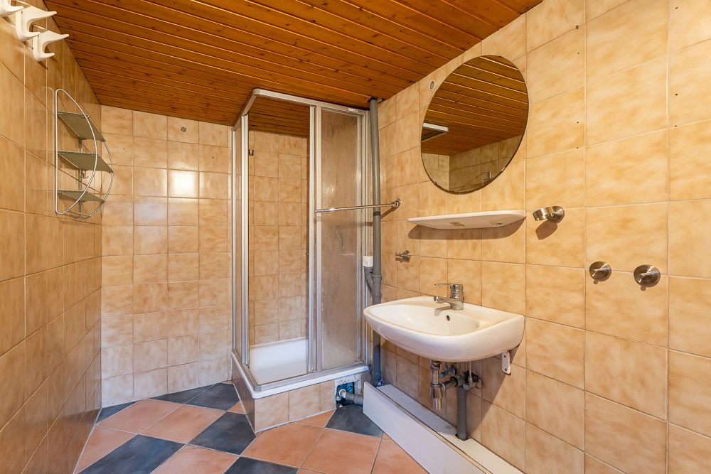 Badezimmer mit Dusche, Waschbecken, rundem Spiegel und gefliesten Wänden und Boden.