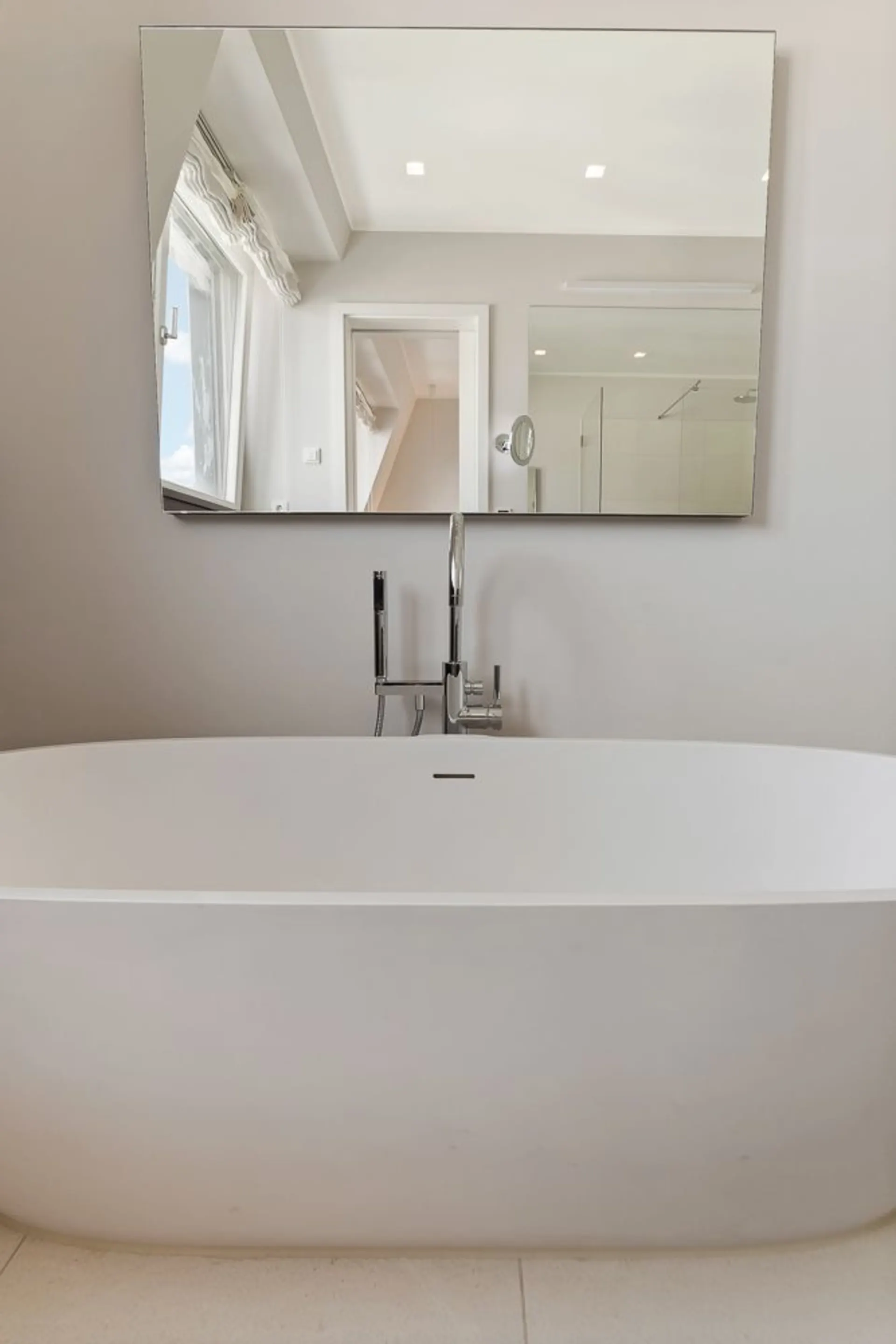 Freistehende Badewanne vor einem großen Spiegel in einem modernen Badezimmer.
