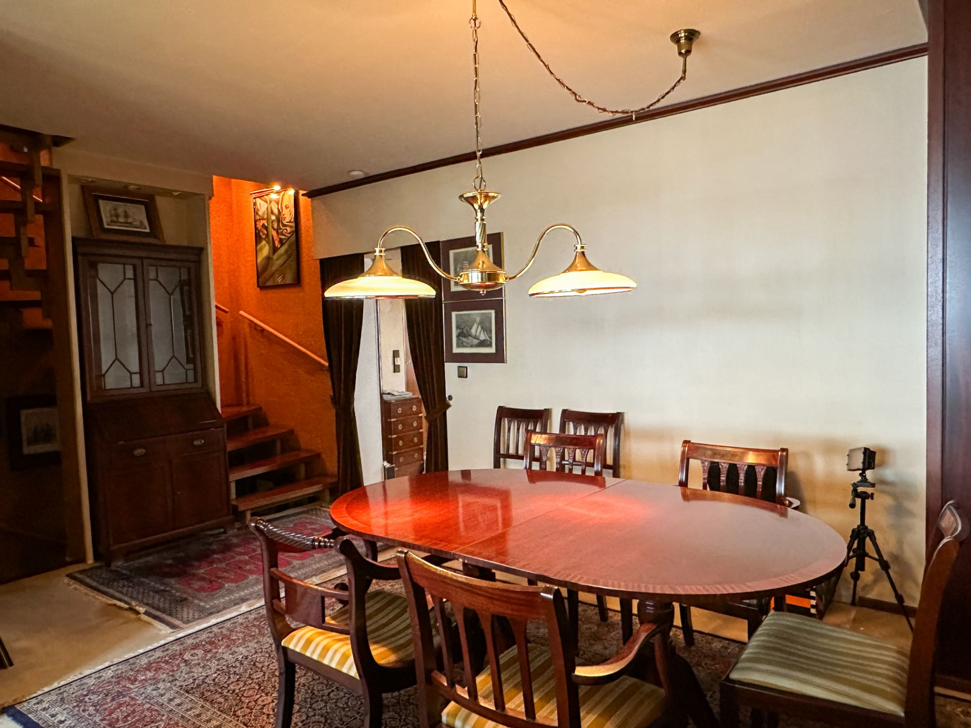 Esszimmer mit ovalem Holztisch, sechs Stühlen, Hängelampe und Holztreppe im Hintergrund.