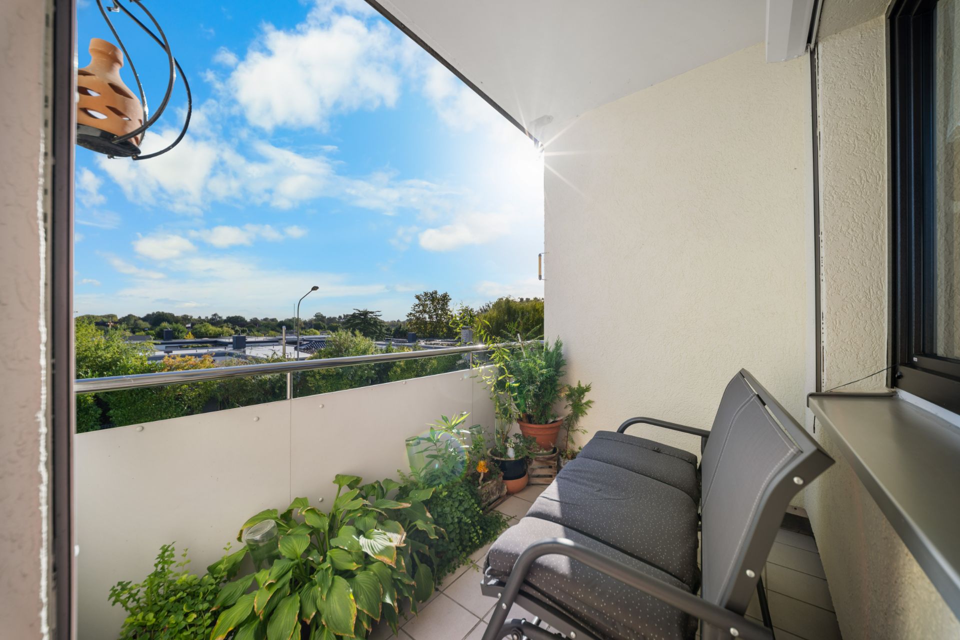 Balkon mit zwei Stühlen, Pflanzen und Ausblick auf Bäume unter blauem Himmel.