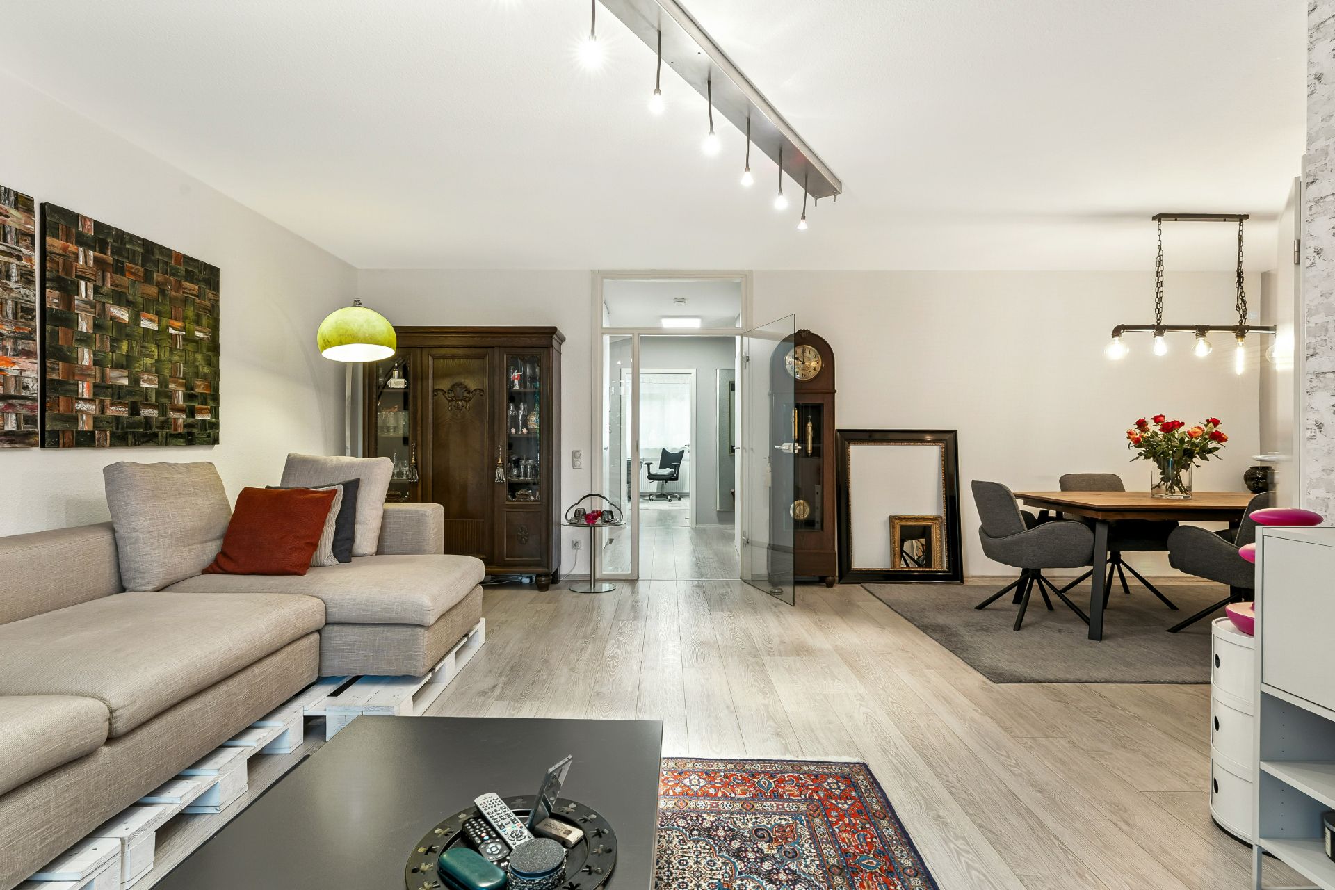 Wohnzimmer mit beiger Eckcouch, Esstisch, Teppich, Schrank und moderner Beleuchtung.