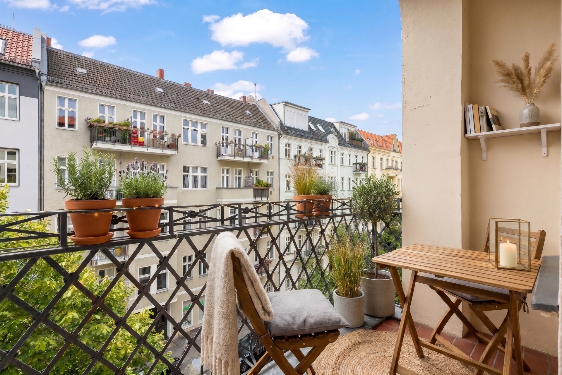 Kleiner Balkon mit Holztisch, Stühlen, Pflanzen und Blick auf Wohnhäuser.