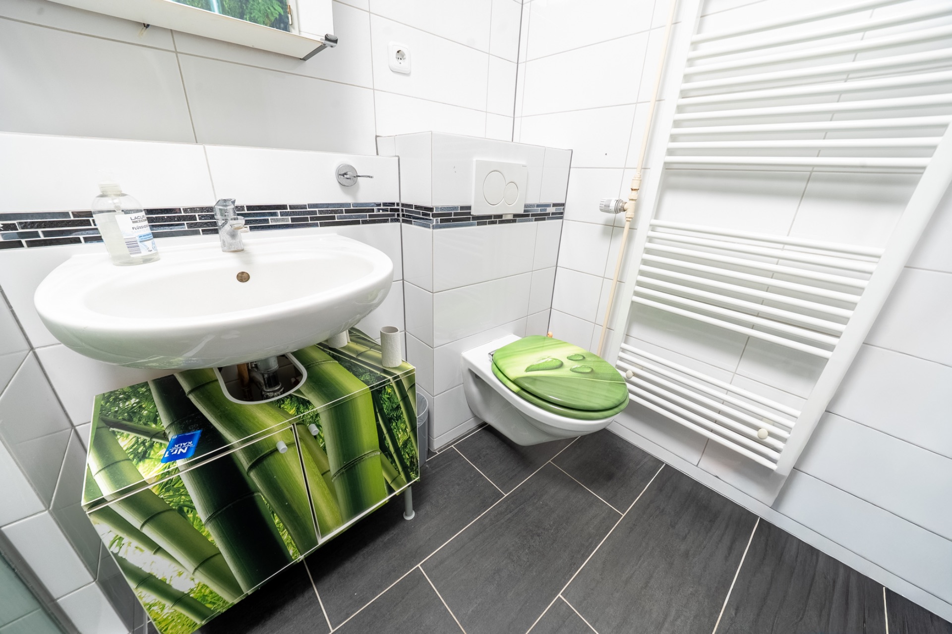 Modernes Badezimmer mit Waschbecken, Toilette und Handtuchheizkörper, Schrank mit Bambusmotiv.