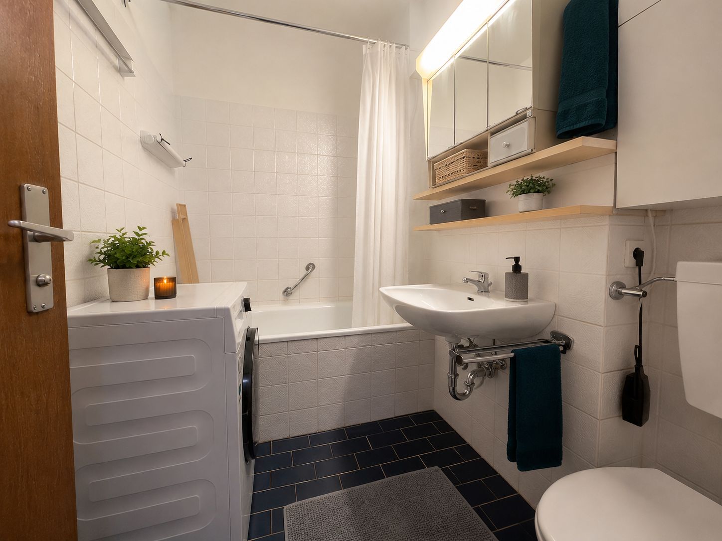 Modernes Badezimmer mit Badewanne, Waschbecken, Waschmaschine und Regal mit Pflanzen.