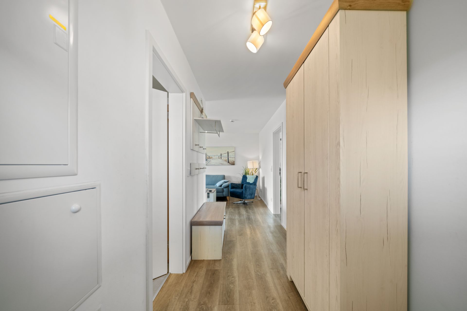 Heller Flur mit Holzschrank, Garderobe und Blick ins Wohnzimmer mit blauen Möbeln.