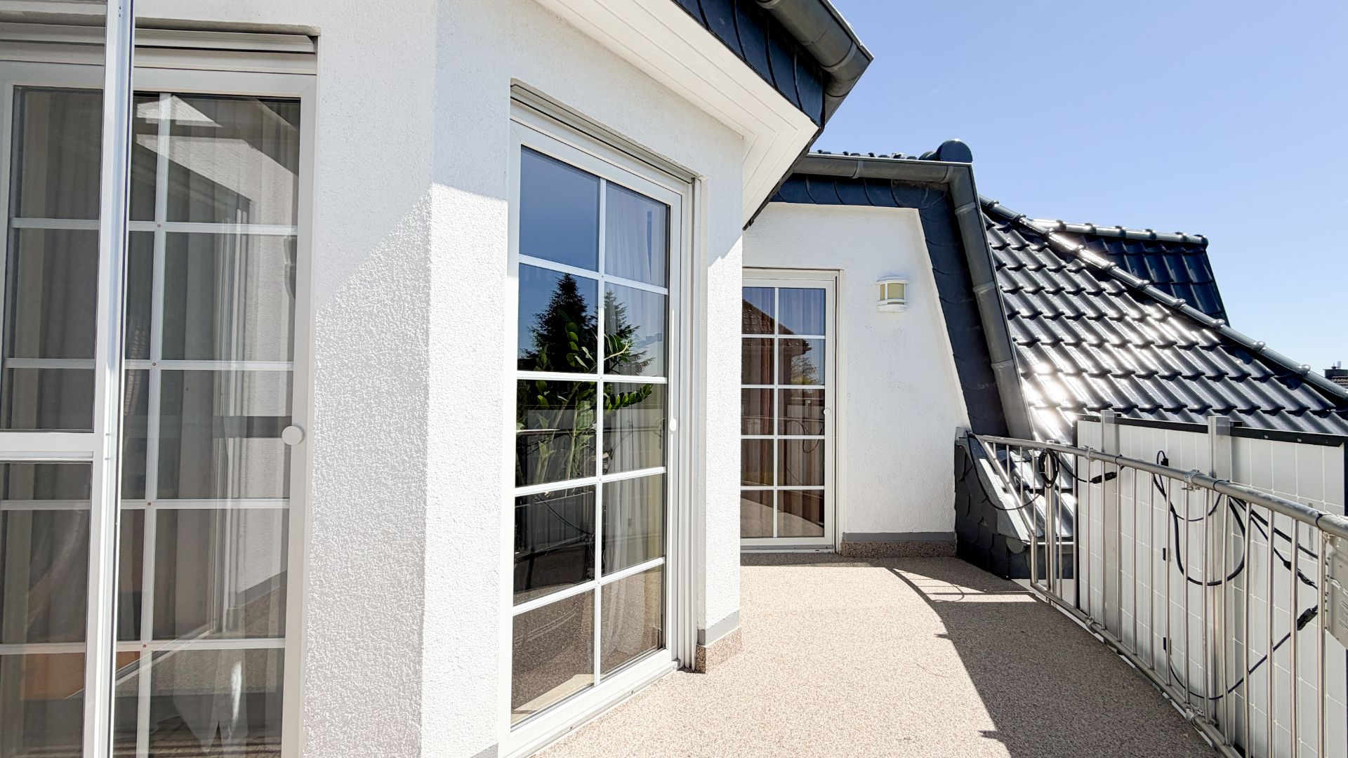 Sonnige Dachterrasse mit weißem Geländer und großen Glas-Schiebetüren.