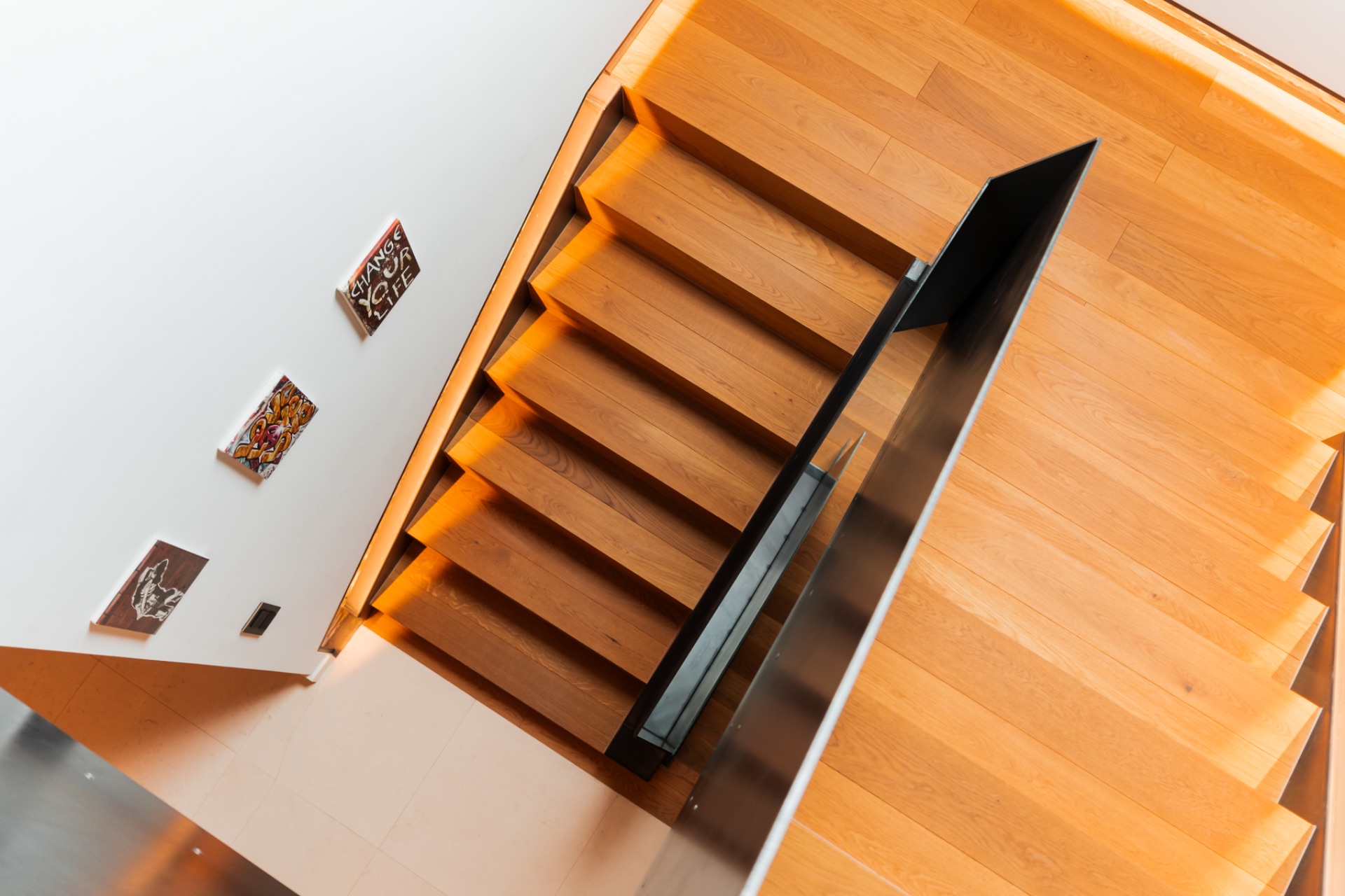 Holztreppe mit schwarzem Geländer und kleinen Bildern an einer weißen Wand.