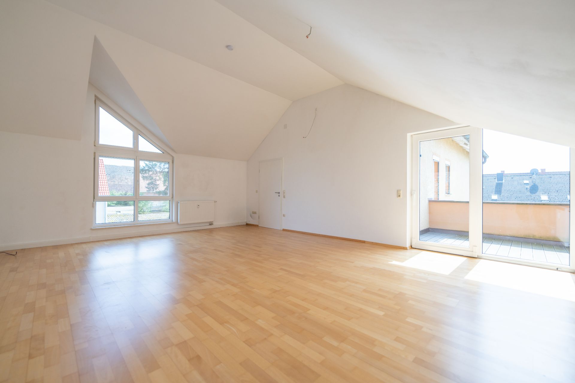 Heller leerer Raum mit Holzfußboden, Dachschrägen und Zugang zu einem Balkon.