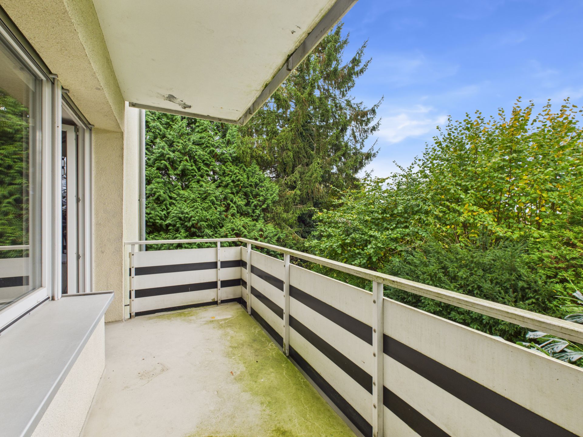 Balkon mit Geländer und Blick auf grüne Bäume und blauen Himmel.