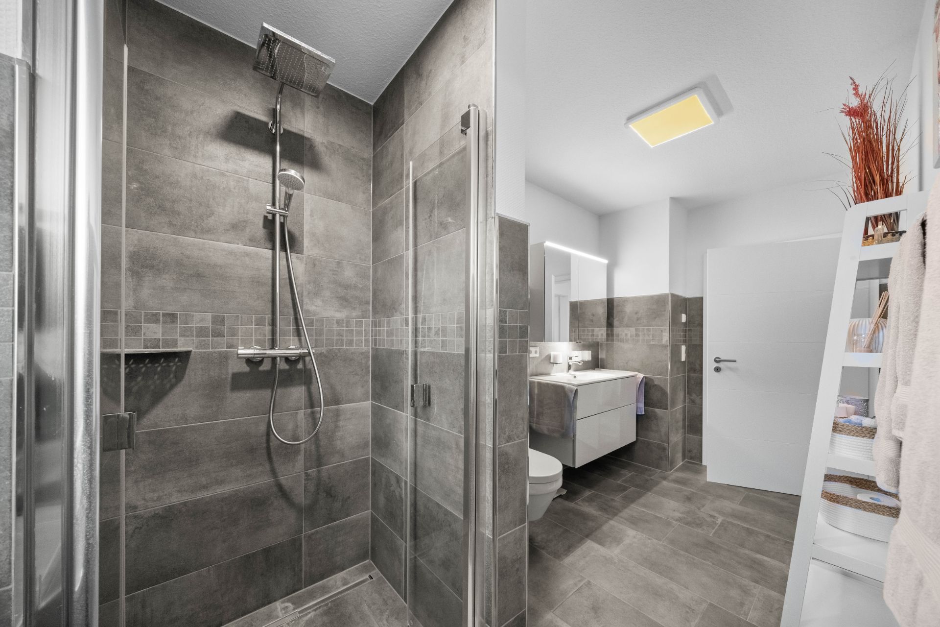 Modernes Bad mit großer Dusche, Spiegel, Waschbecken, Regal und Handtüchern.
