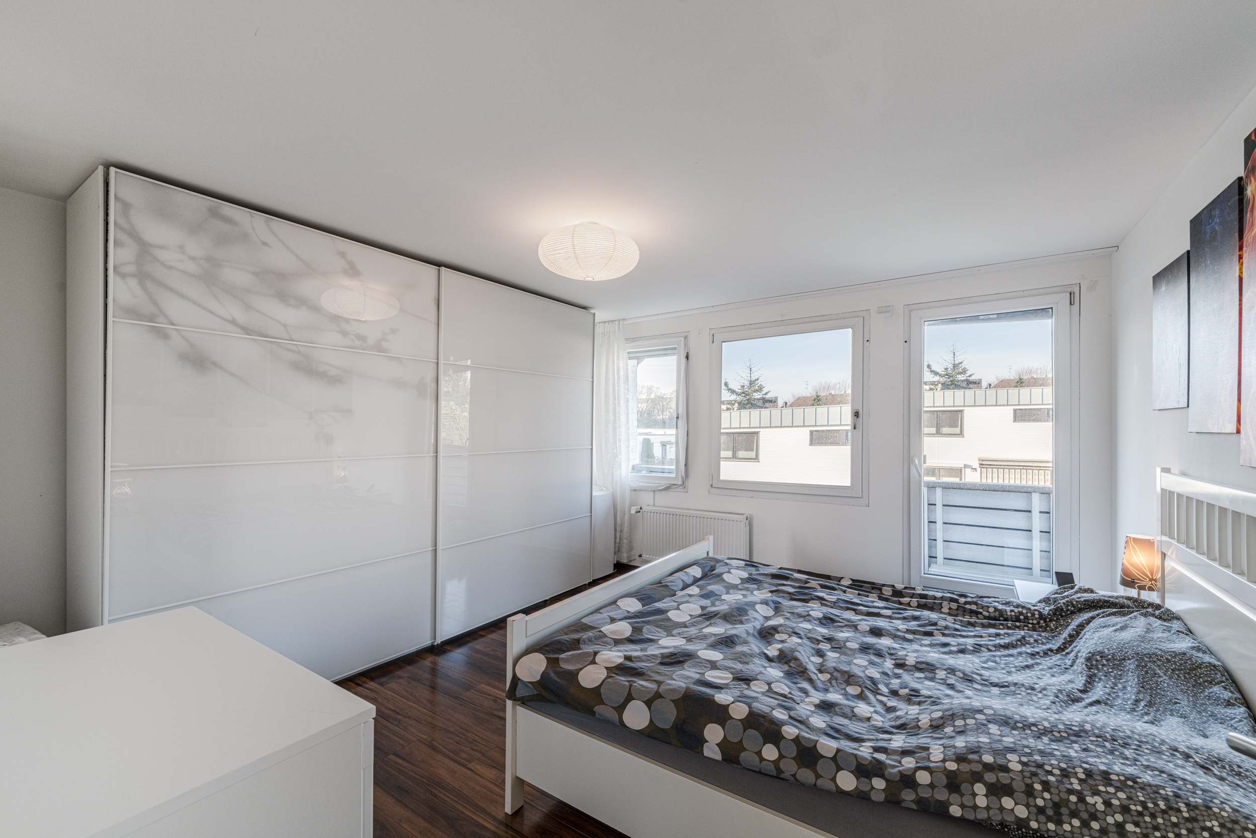 Helles Schlafzimmer mit Doppelbett, großem weißen Kleiderschrank und Fenster mit Blick nach draußen.