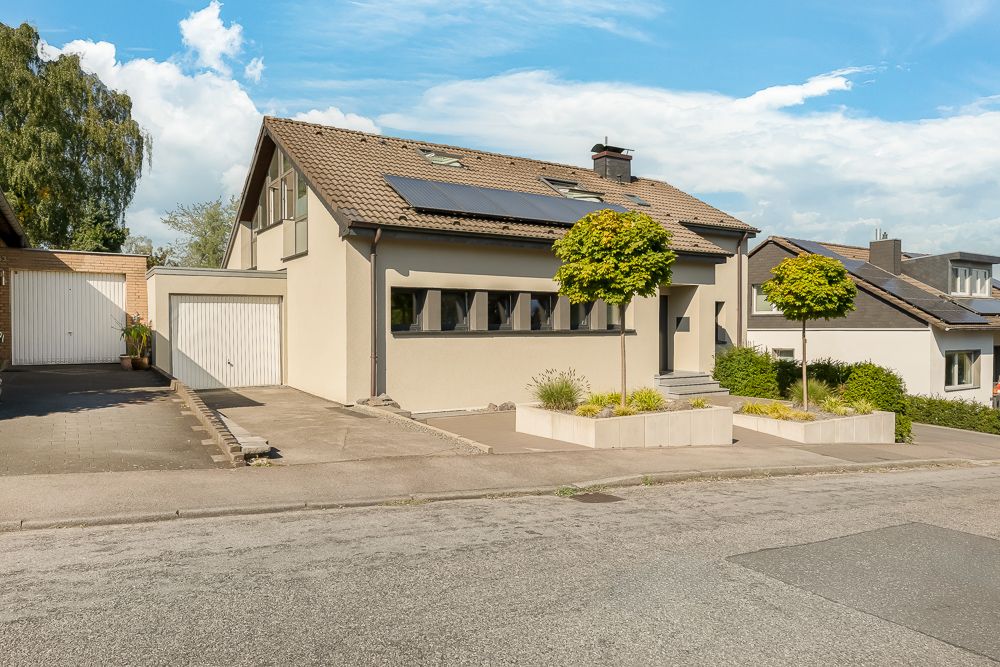 Modernes Einfamilienhaus mit Garage, Vorgarten und zwei kleinen Bäumen vor dem Eingang.