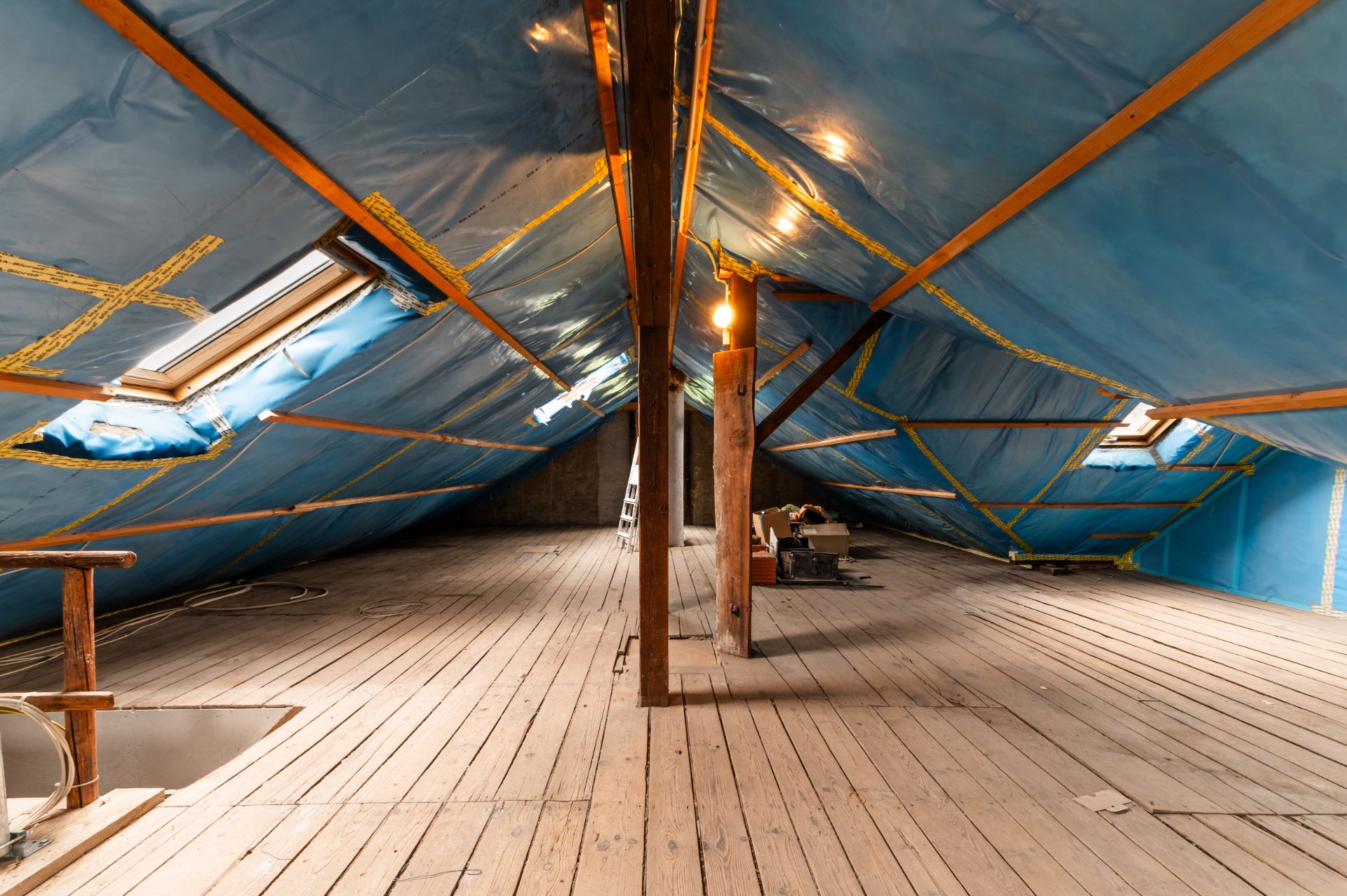 Geräumiger Dachboden mit Holzfußboden, sichtbaren Balken und blauer Folienisolierung.