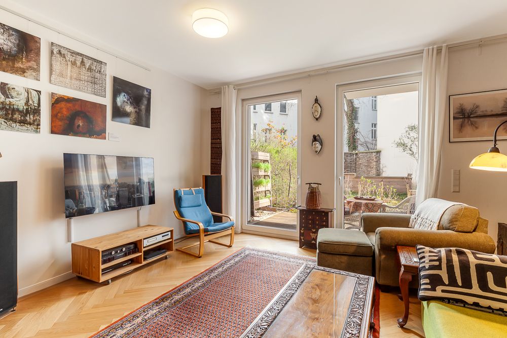 Wohnzimmer mit Sofa, Sessel, Teppich, TV, Wandkunst und Zugang zur Terrasse.