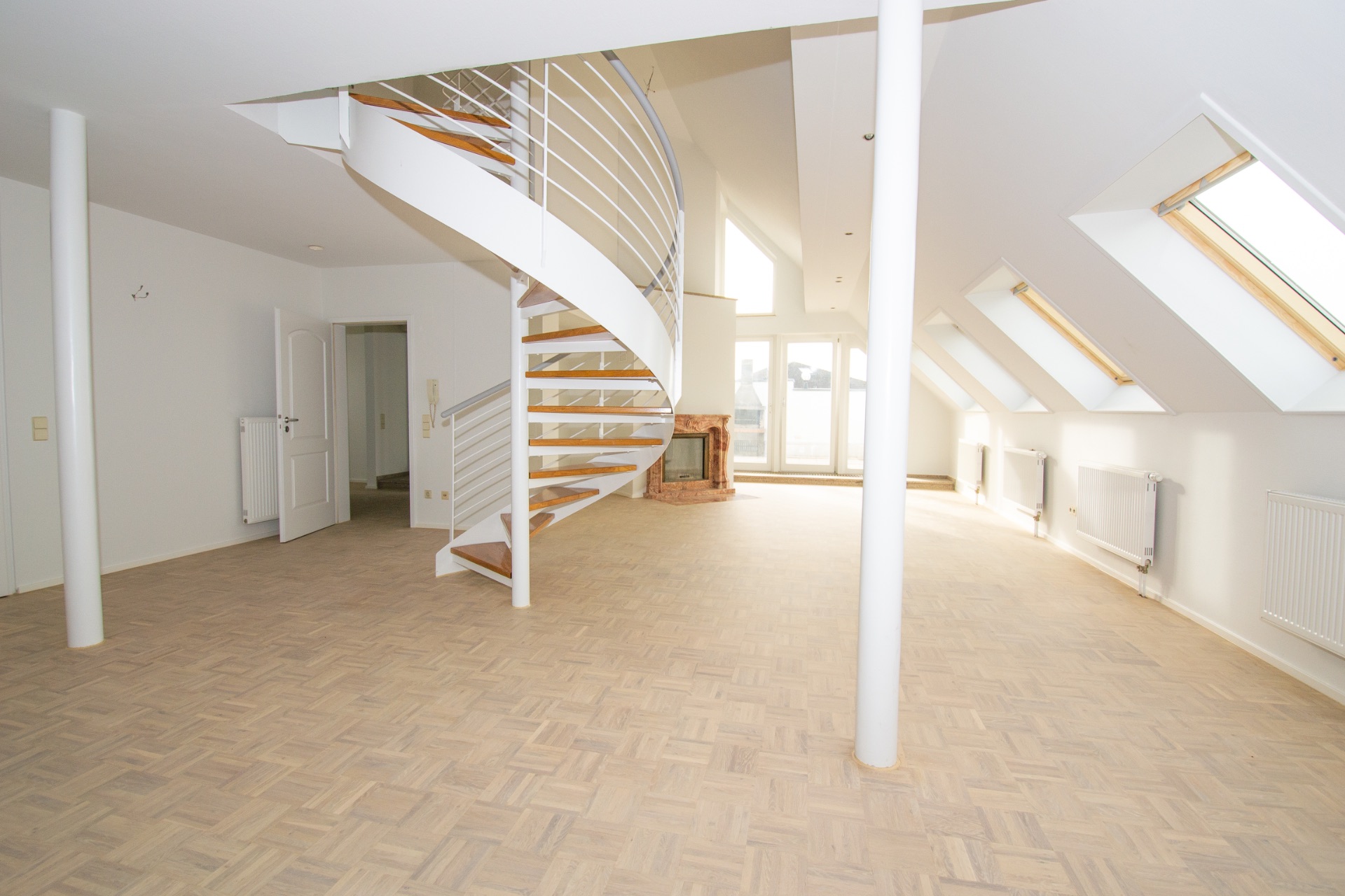 Helles Wohnzimmer mit Holzfußboden, Kamin, Wendeltreppe und mehreren Dachfenstern.