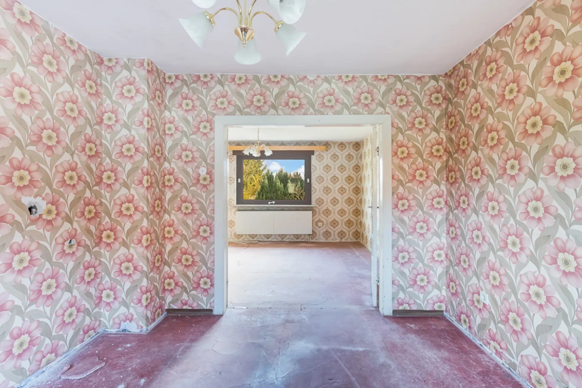 Zimmer mit rosa-blumiger Tapete und Blick in einen weiteren Raum mit gemusterter Tapete.