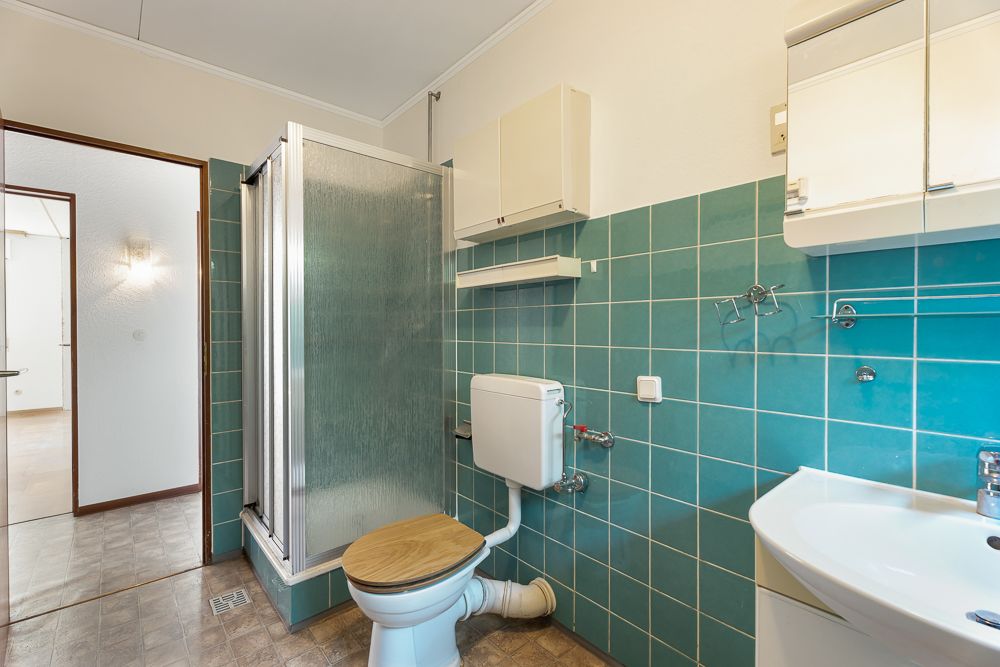 Badezimmer mit grünen Fliesen, Dusche, Toilette und Waschbecken.