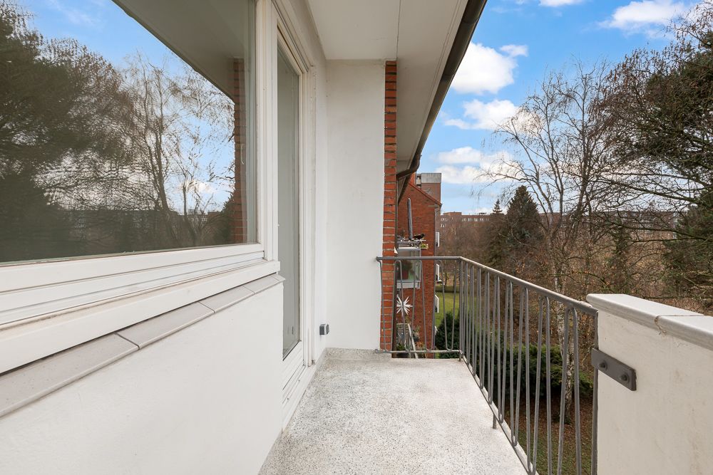 Balkon mit Geländer und Blick auf Bäume und Nachbarhäuser an einem sonnigen Tag.