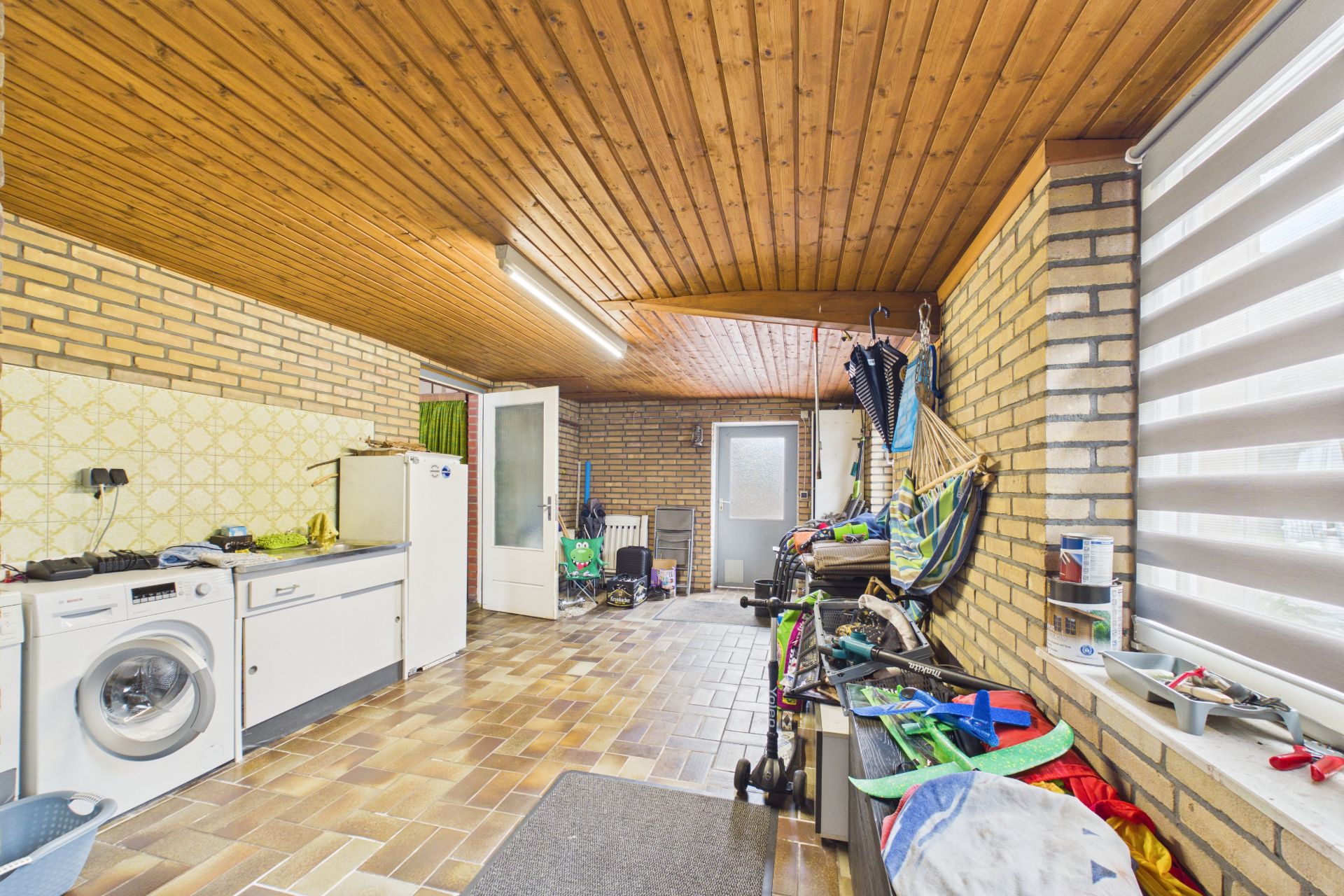 Hauswirtschaftsraum mit Waschmaschine, Spüle, Regalen und sichtbaren Haushaltsgegenständen.