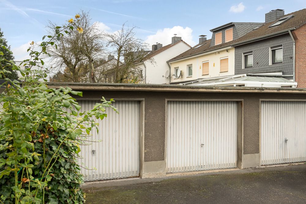 Drei Garagentore vor einem Wohnhaus mit etwas Bewuchs an der Seite.