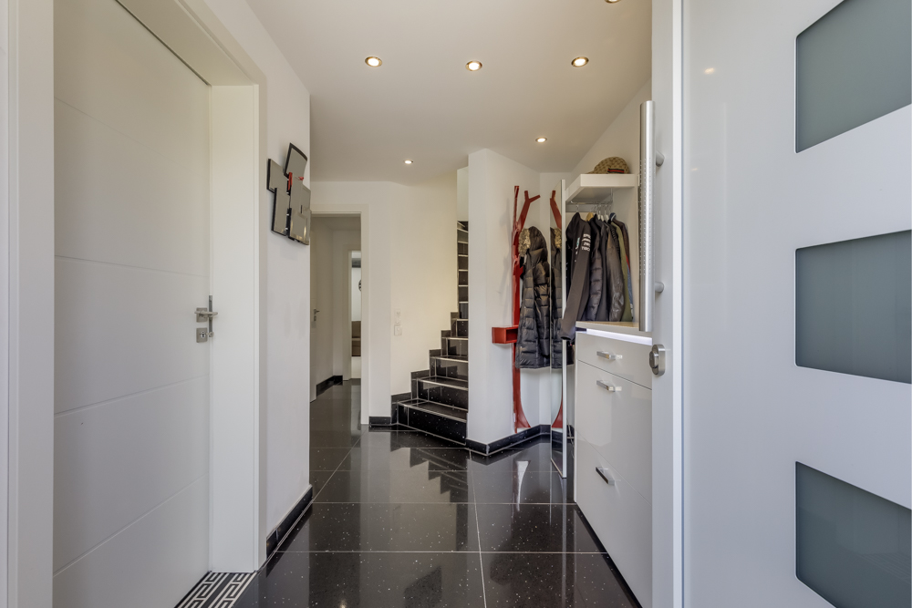 Moderner Flur mit Treppe, Garderobe und schwarzem Fliesenboden in einem Wohnhaus.