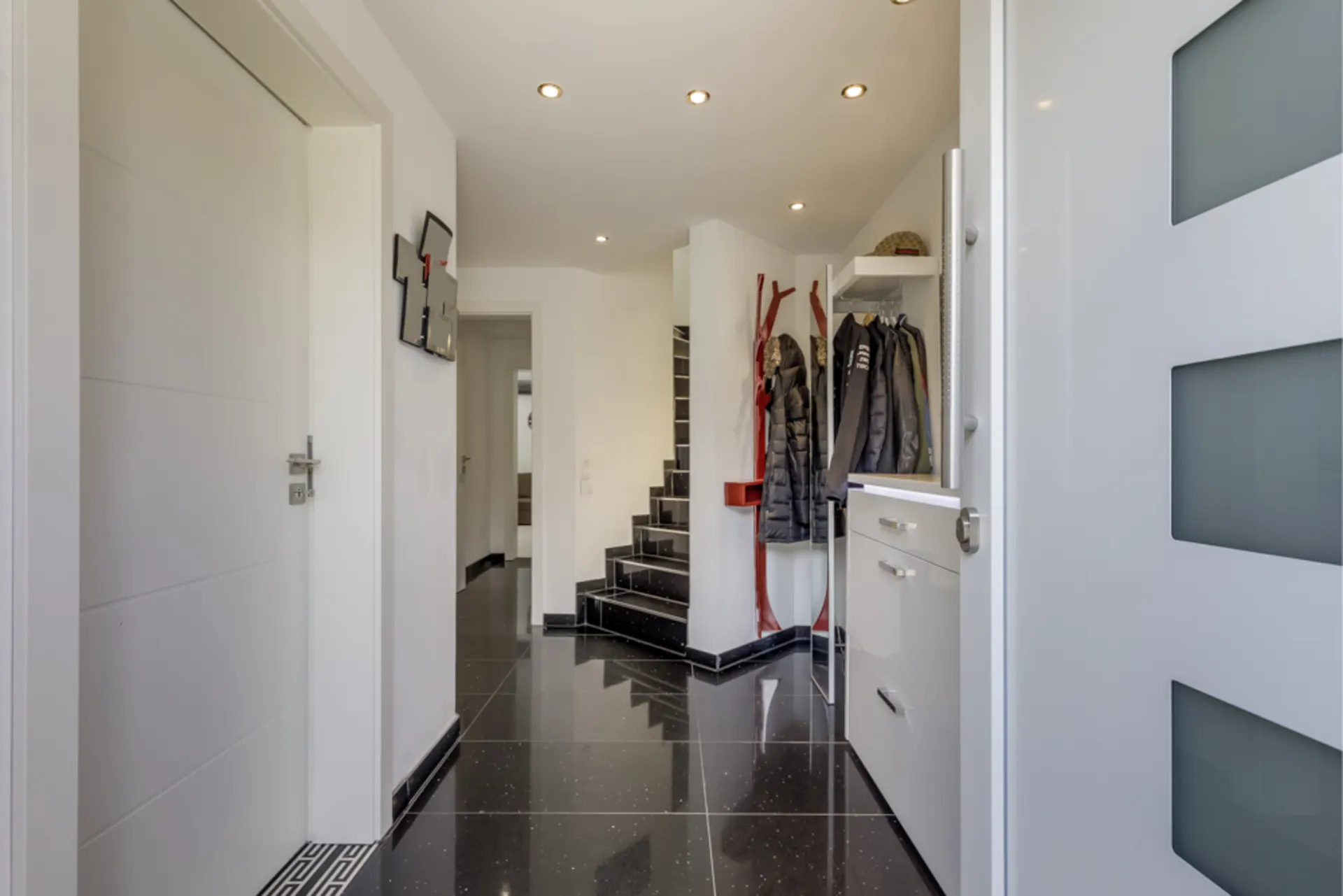 Moderner Flur mit Treppe, Garderobe und schwarzem Fliesenboden in einem Wohnhaus.