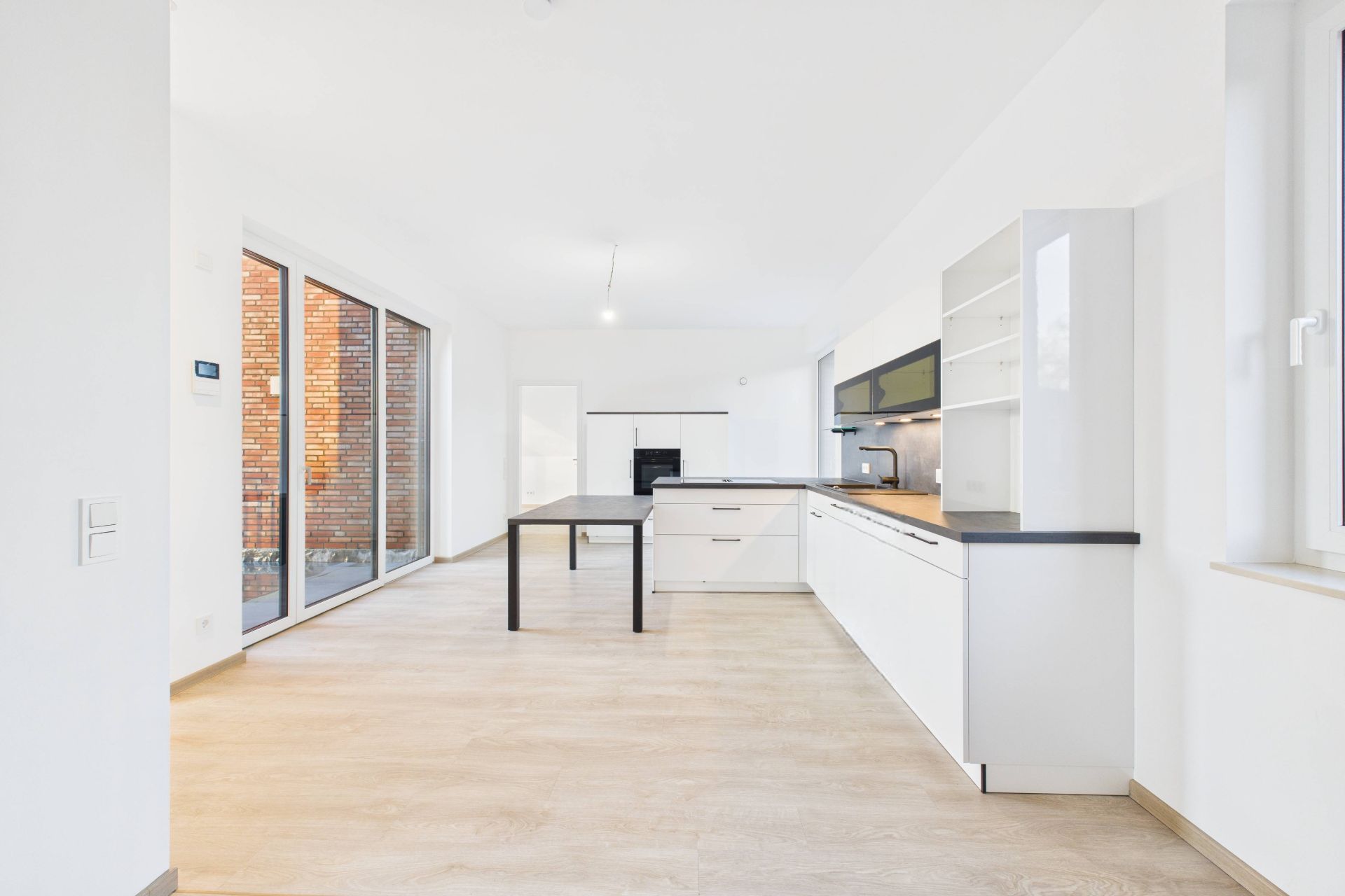 Helle, moderne Küche mit Holzboden, weißen Schränken und großen Fenstern.