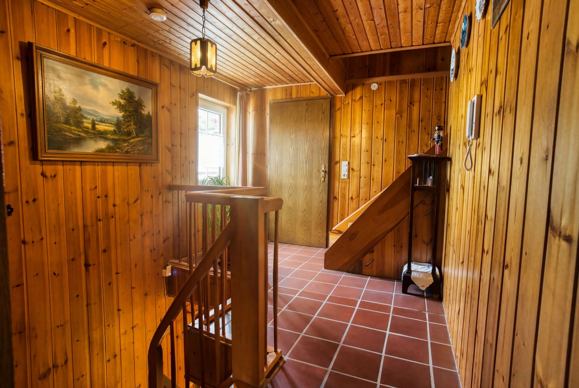 Hausflur mit Holzvertäfelung, Treppe, Bild an der Wand und Fliesenboden.