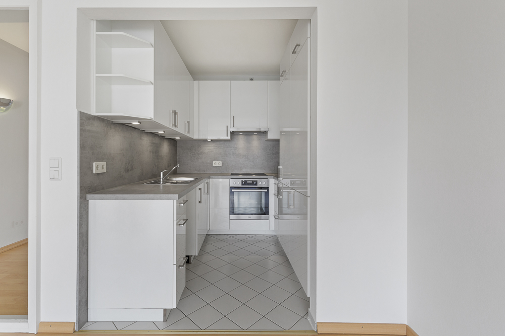 Moderne Einbauküche mit weißen Schränken, grauer Arbeitsplatte und Fliesenboden.