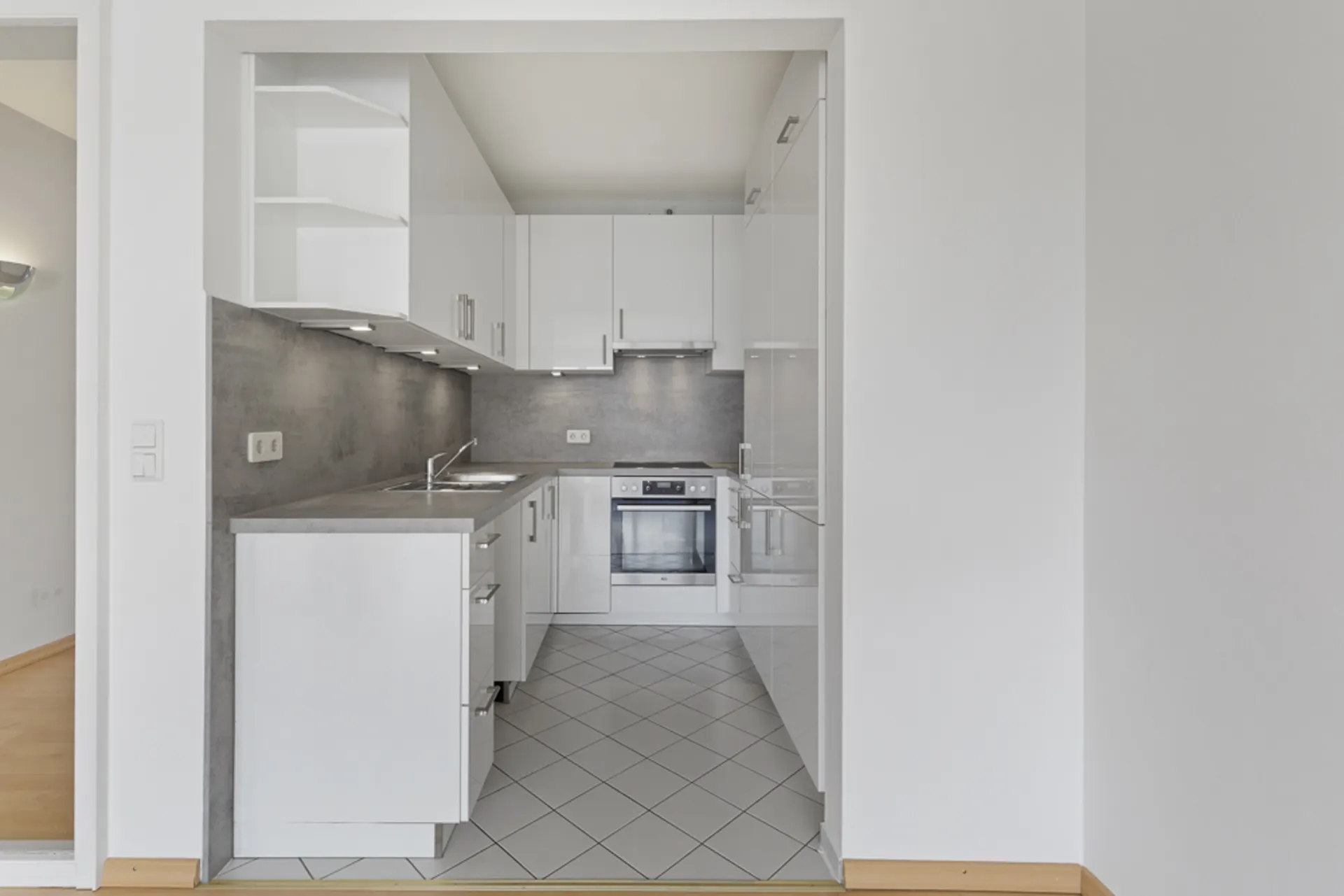 Moderne Einbauküche mit weißen Schränken, grauer Arbeitsplatte und Fliesenboden.