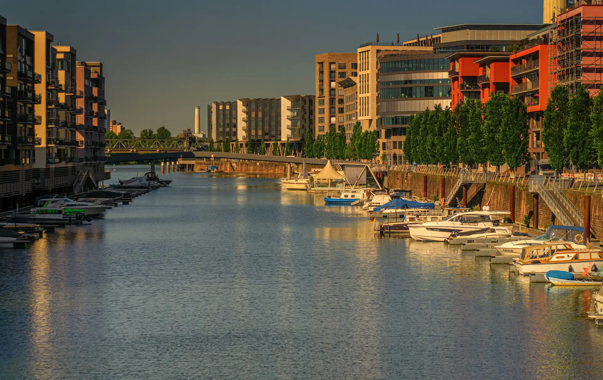 Moderne Wohngebäude am Wasser mit Booten und Bäumen an beiden Ufern bei Sonnenlicht.