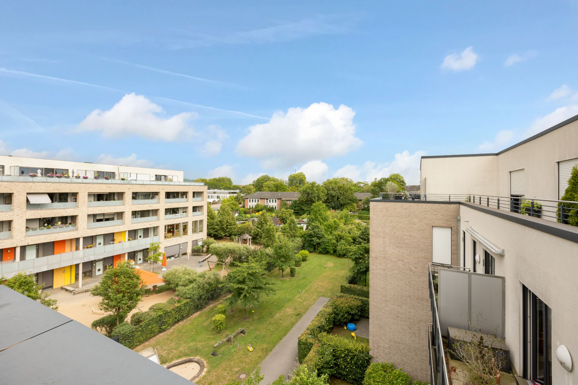 Blick auf einen begrünten Innenhof zwischen modernen Wohngebäuden bei Tageslicht.