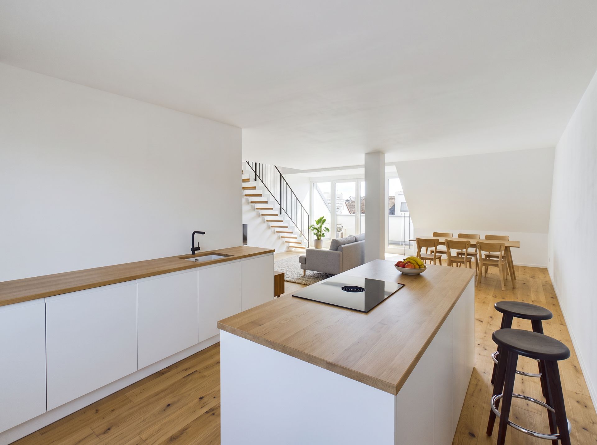 Moderne offene Küche mit Holzboden, Esstisch, Wohnzimmer und Treppe im Hintergrund.